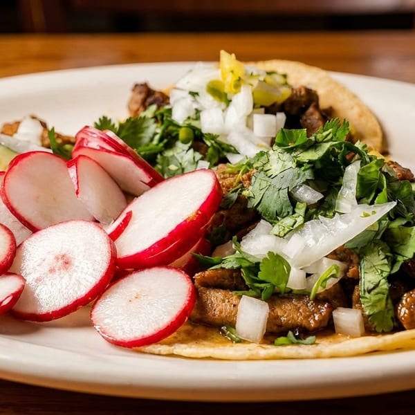 Two street tacos topped with seasoned meat, cilantro, onions, and sliced radishes on a white plate.