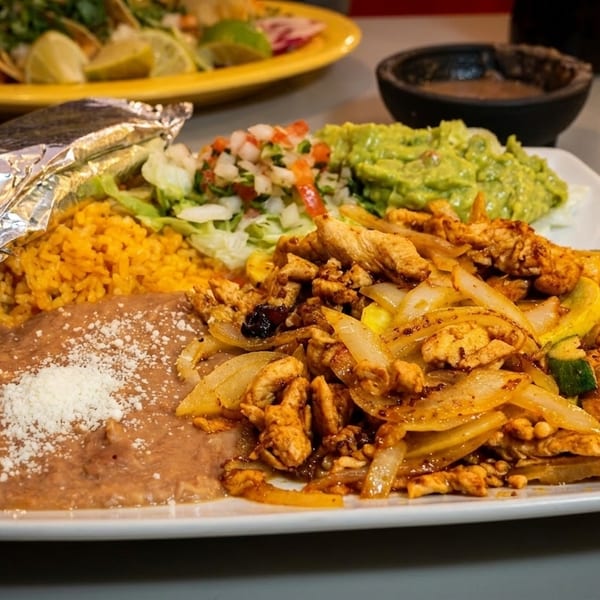 Large plate of chicken fajitas, rice, refried beans, guacamole, pico de gallo, and a foil-wrapped item.